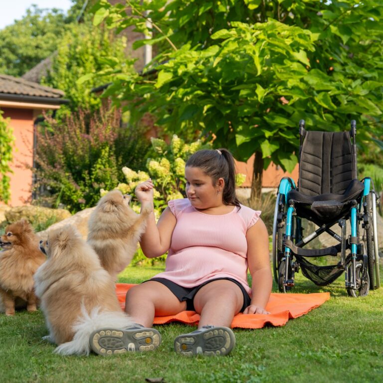 Erika Beranová sedí na dece na zahradě se svými psy, vedle stojí její vozík